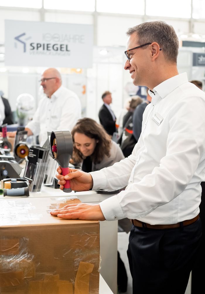 Christian Schröder von envirogroup zeigt Kunden auf der Fachpack 2022 wie der zerotape Handabroller funktioniert